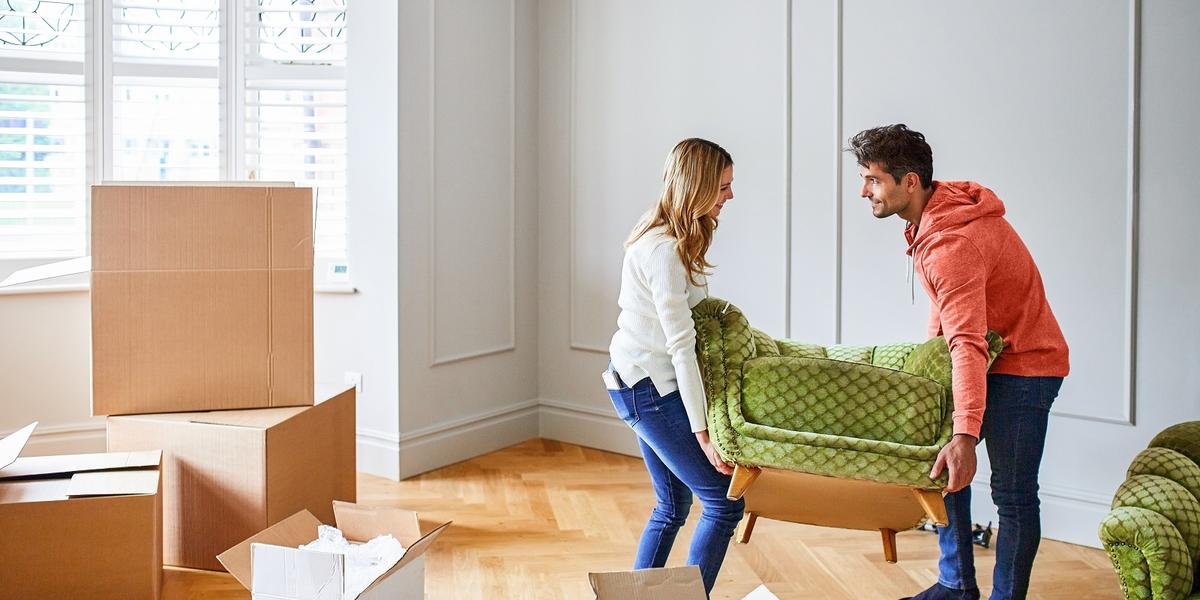 Man en vrouw dragen een groene stoel in hun woonkamer tijdens het verhuizen