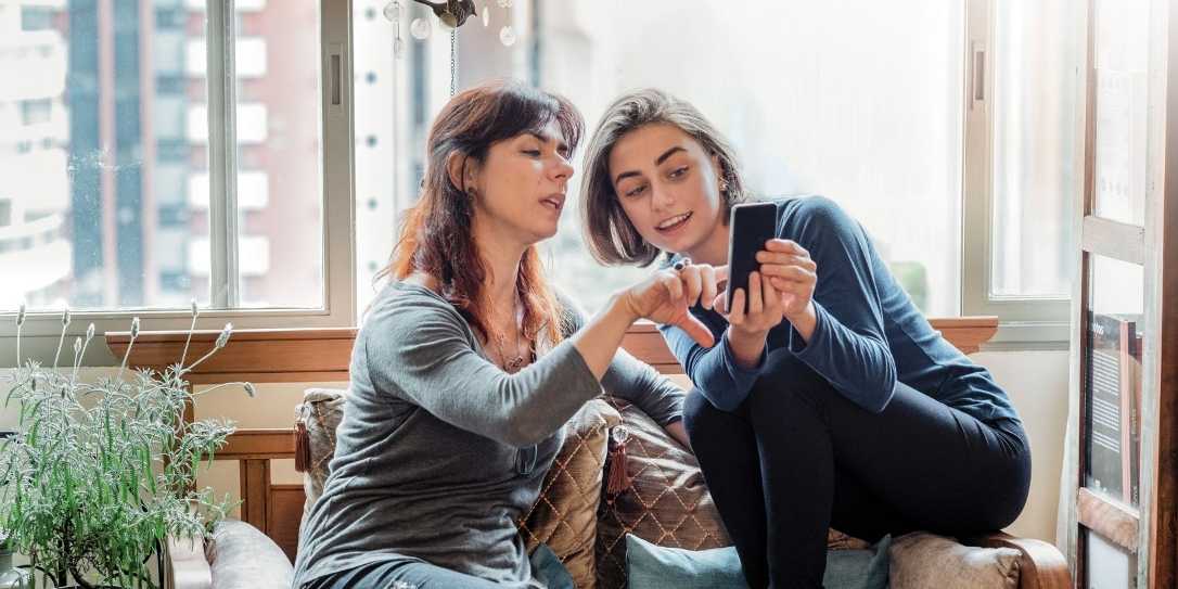 Twee vrouwen zitten in de woonkamer op een telefoon te kijken