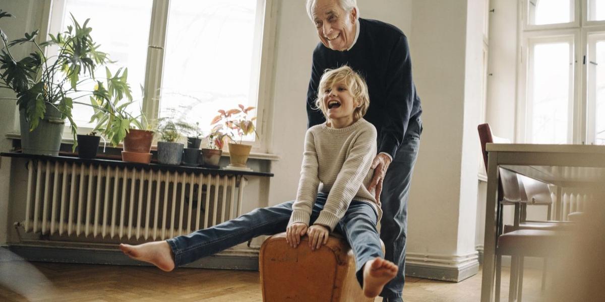 Opa en kleinzoon spelen lachend samen in woonkamer met planten in de vensterbank.